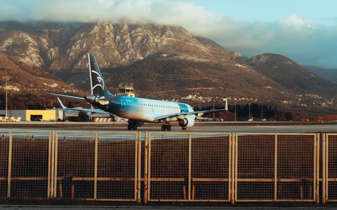 Ein Verkehrsflugzeug auf der Startbahn des Flughafens Tivat, dahinter Kontrollturm und felsige Berge