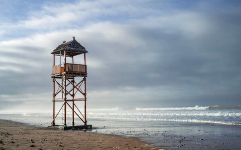 A wooden lifeguard tower on an empty sandy beach at Agadir, with waves and a dramatic cloudy sky