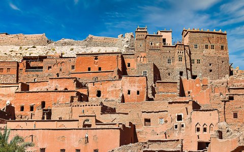 The earthen clay houses and towers of the Ait Benhaddou kasbah climbing a hill, under a clear blue sky