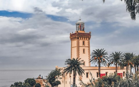 Leuchtturm am Kap Spartel zwischen Palmen über dem Meer bei Tanger unter grauen und weißen Wolken
