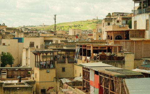 A view across the flat rooftops and old buildings of the Fes medina, under a blue sky with white clouds