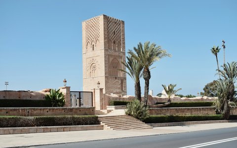 Steinerner Hassan-Turm neben Palmen und einer breiten Straße in Rabat unter klarem blauem Himmel