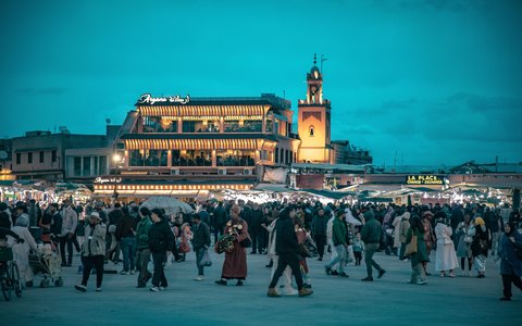 Crowds in Jemaa el-Fnaa square at dusk in front of lit cafe terraces, under a deep blue evening sky