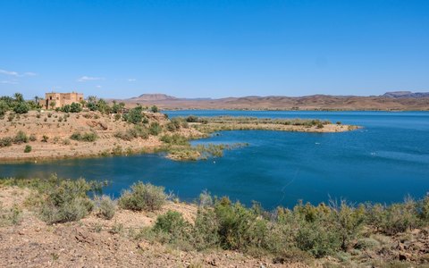 The blue water of the lake at Ouarzazate surrounded by dry desert hills, under a blue sky