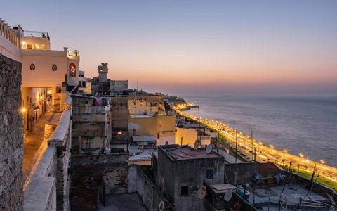 Rooftops of the Tangier medina at dusk, above the lit seafront road along the bay