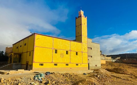 A bright yellow mosque with a square minaret under a blue sky with white clouds in Taroudant
