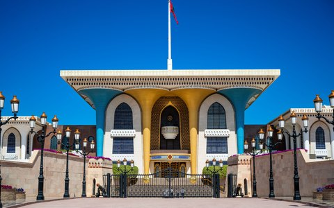 The blue and gold facade of Al Alam Palace in Old Muscat behind its gates, under a deep blue sky