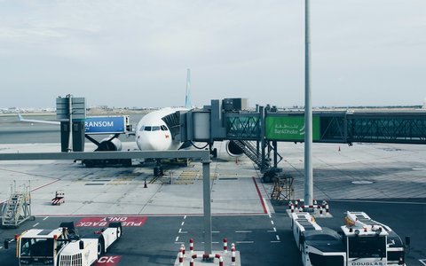 Verkehrsflugzeug an einer Fluggastbrücke auf dem Vorfeld des Flughafens Maskat, davor Servicefahrzeuge