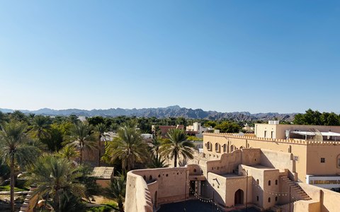 Nizwa Fort and the palm oasis around it with the Hajar Mountains behind, under a clear blue sky