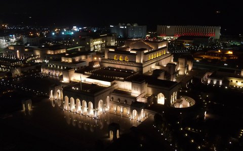 Aerial night view of the lit-up Royal Opera House Muscat and its gardens