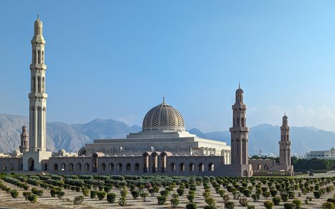 The domes and tall minarets of the Sultan Qaboos Grand Mosque against a clear blue sky