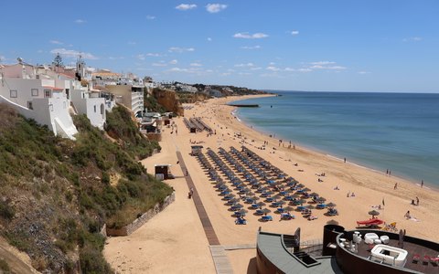 Albufeira beach below sandstone cliffs and white buildings, with blue sea and a clear sky