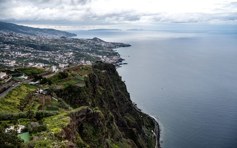 Aerial view of the cliffs and town of Camara de Lobos beside the Atlantic, with Funchal along the coast beyond