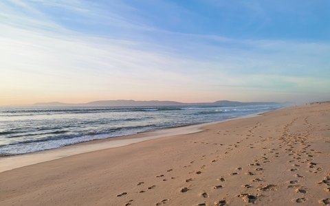An empty sandy beach with footprints and gentle waves at Comporta in soft sunset light