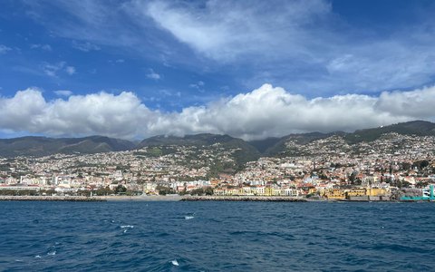 Funchal spread across green hills above the blue ocean, with white clouds over the mountains