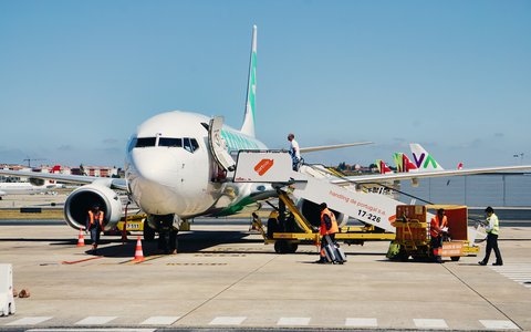 Bodenpersonal lädt Gepäck in ein weißes Verkehrsflugzeug mit Gangway auf dem Vorfeld des Flughafens Lissabon