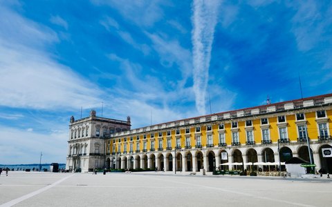 The yellow arcaded buildings and triumphal arch of Praca do Comercio in Lisbon, under a vivid blue sky