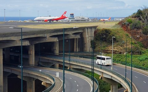 Erhöhte Landebahn auf Betonpfeilern über der Straße am Flughafen Madeira, dahinter ein Verkehrsflugzeug und das Terminal