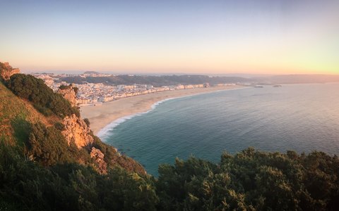 The long beach and town of Nazare curving along the bay in warm sunset light, seen from the cliff top