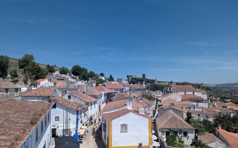 White houses with red tiled roofs inside the old walled village of Obidos, under a blue sky