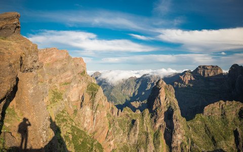 Jagged volcanic peaks and ridges seen from Pico do Arieiro, with clouds below and a blue sky