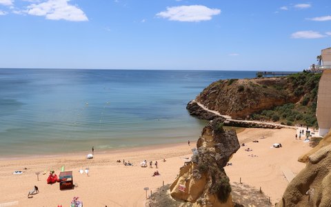 The wide sandy beach of Praia da Rocha below golden cliffs, with blue sea and a few clouds