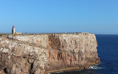 A lighthouse at the edge of a sheer cliff at Sagres Point above a deep blue sea