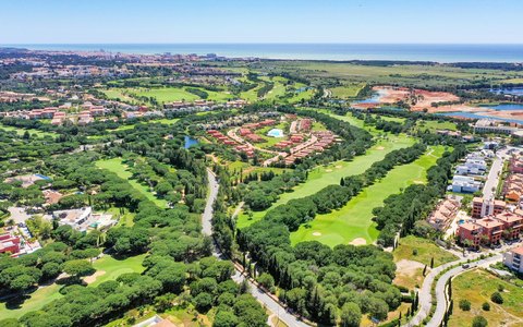 Aerial view of green golf fairways and pine trees among the villas of Vilamoura, with the sea on the horizon