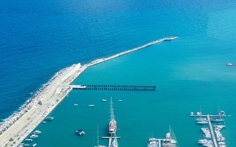 Aerial view of a long harbour wall and moored boats in clear turquoise water at Castellammare del Golfo