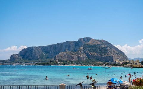 Turquoise water at Mondello beach with the rocky bulk of Monte Pellegrino behind, under a blue sky with a few clouds
