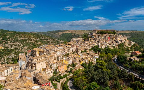 Aerial view of the old hilltop town of Ragusa Ibla with its domes among green hills, under a blue sky