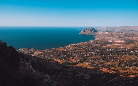 A high view down to the coastal plain and bay of San Vito Lo Capo with a headland and the blue sea beyond