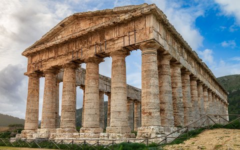 The Doric temple of Segesta standing on a green hillside under a blue sky with white clouds