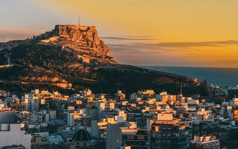 Dächer von Alicante unter einem felsigen Hügel mit Burg im warmen Abendlicht