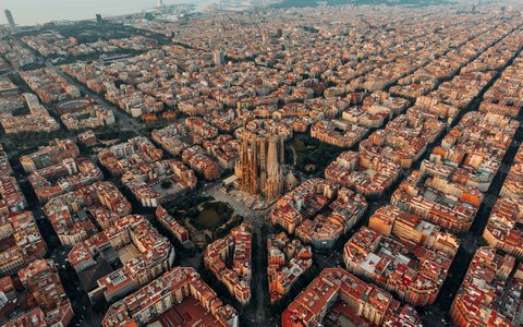 Luftbild der schachbrettartig angeordneten Häuserblöcke Barcelonas, aus deren Mitte die Sagrada Família aufragt