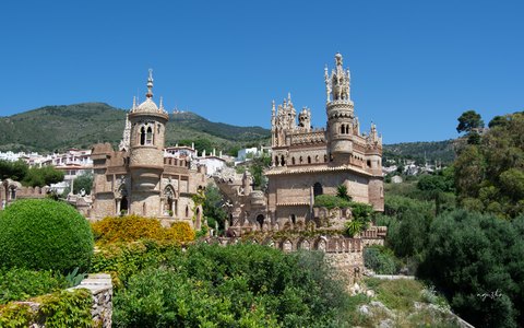 The ornate stone towers of the Castillo de Colomares above green gardens, under a bright blue sky