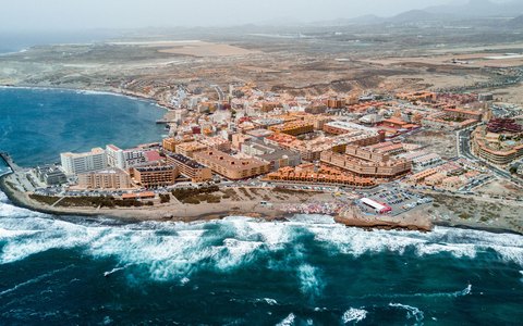 Aerial view of the town of El Medano along the shore, with waves breaking on the rocks and the plain behind