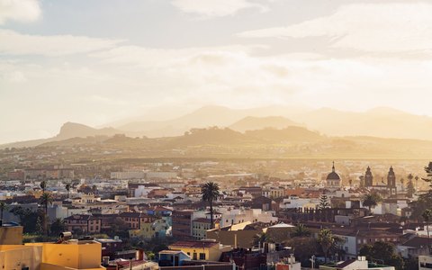 The rooftops and church towers of La Laguna with mountains behind in warm early light