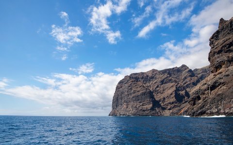 The sheer dark cliffs of Los Gigantes rising from the ocean, with white clouds in a vivid blue sky