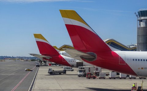 Rote und gelbe Flugzeugleitwerke auf dem Vorfeld des Flughafens Madrid, dahinter der Kontrollturm