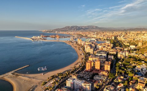 Aerial view of Malaga's harbour, beaches and city in bright sunlight, with mountains behind