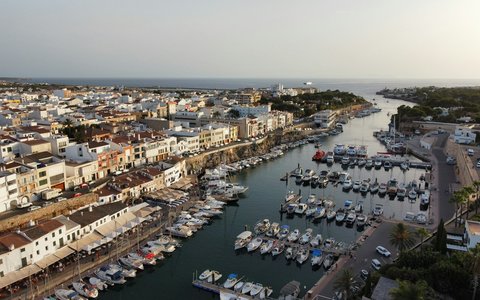 Luftbild des langen Hafens von Ciutadella auf Menorca, gesäumt von Booten und weißen Häusern