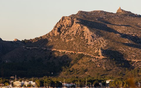 Sailboats on calm water in front of the rocky hills of Port de Pollenca in warm evening light