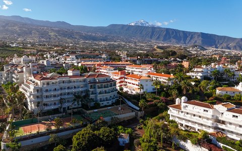 Aerial view of the white buildings of Puerto de la Cruz with green slopes and Mount Teide behind