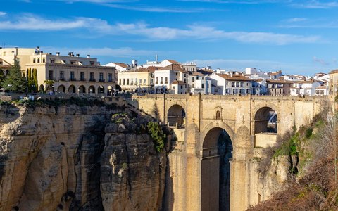 The Puente Nuevo bridge spanning the deep gorge at Ronda, with white buildings on the cliff top under a blue sky