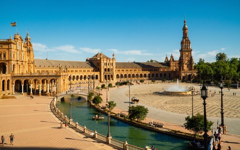 Geschwungene Backsteingebäude, Turm und Kanal der Plaza de España in Sevilla bei strahlender Sonne