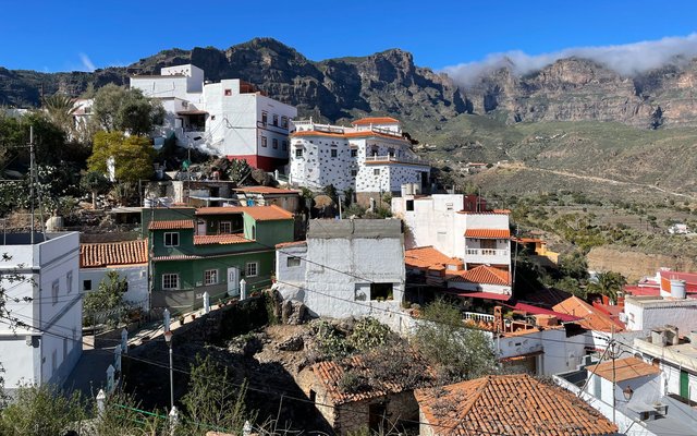 White and colourful houses with tiled roofs on a hillside in Tejeda, below rugged mountains and a blue sky