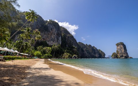 Sandy Ao Nang Beach with palm trees, limestone cliffs and a rock stack offshore