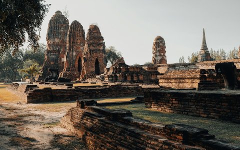 Brick temple towers and low ruined walls on dry grass under a pale sky