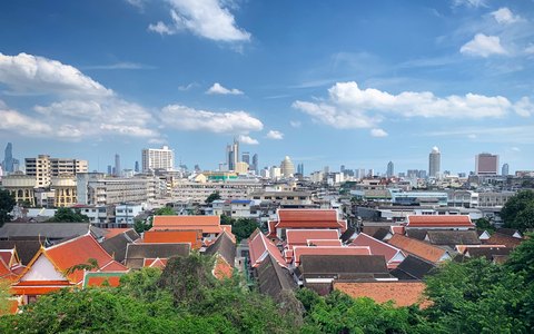 Traditional Thai temple roofs in front of Bangkok's modern skyline, under a blue sky with white clouds